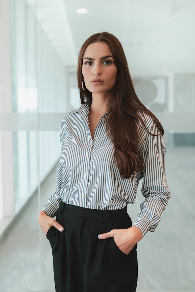 Businesswoman with brown hair in a striped shirt standing confidently in an office.
